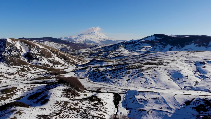 Aerial shot with drone of the Nebrodi mountains in winter with a view of smoking Etna and Lake Pisciotto. Winter in Sicily. Snow in Sicily. Snow-capped Etna. Iced lake.