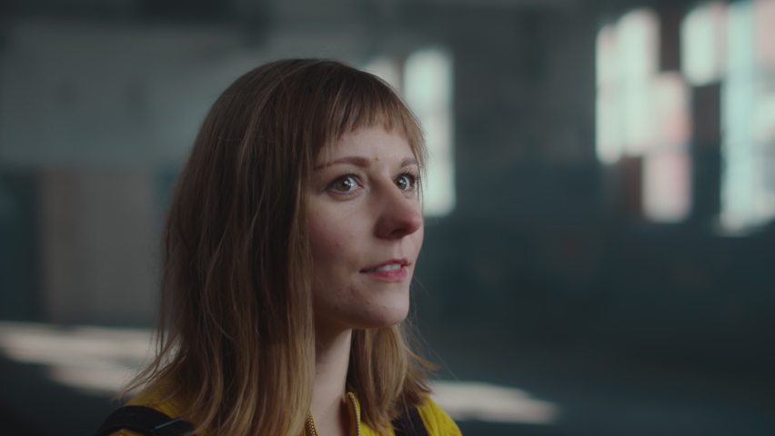 Isolated Beautiful Caucasian Female Artist Looking At Her Finished Job Proud and Excited, Wiping Her Face With Her Hand Leaving a Paint Mark on it, Working in an Abandoned Art Studio Building.