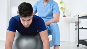 Physiotherapist helps handsome young patient for doing pilates exercises with ball. High quality 4k footage