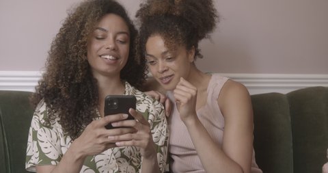 Two female friends laughing whilst using a smartphone