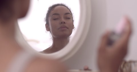 Young adult female looking at her reflection in a mirror and hydrating mist