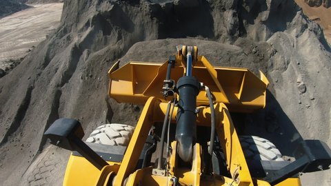 Excavator bucket scoops rubble. Yellow wheel loader picks up and moves crushed stone. Heavy machinery working on quarry or construction site. Onboard POV camera footage