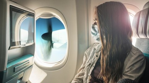 A young woman wearing face mask during travel with airplane , New normal journey after covid-19 pandemic concept. Cinemagraph. Still picture with moving propeller