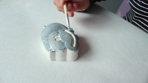 A little curly girl of European appearance of 3-4 years old paints a plaster figure of a hippo. Home hobby and fun game.
