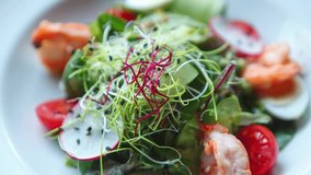 Stock food video of fresh seafood salad with shrimps and microgreens served on white plate on table in Mediterranean restaurant, filmed in 4K ultra hd