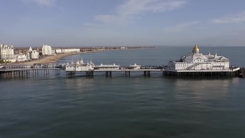 Eastbourne Pier and the Seafront at this popular resort town in East Sussex on a warm and calm sunny day. Aerial footage.