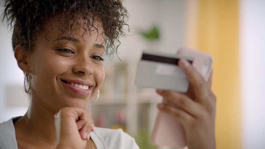 
Happy and Smiling African American Woman Making a Card Payment Through Mobile Phone  Attractive Black Girl Putting Debit or Credit Card Details on a Smartphone. Online Shopping. 
