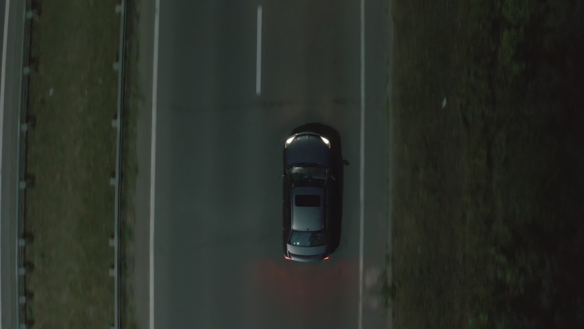 Aerial top down 4k view of dark gray car driving on country road in forest in the evening night. Cinematic drone shot flying over gravel road in pine tree forest. aerial view  Royalty-Free Stock Footage #1082869039