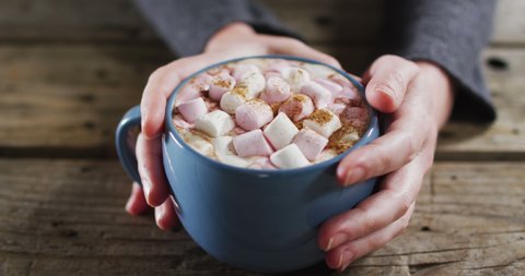 Close up view of hands holding a hot chocolate with marshmallows against wooden surface. thanksgiving festivity concept