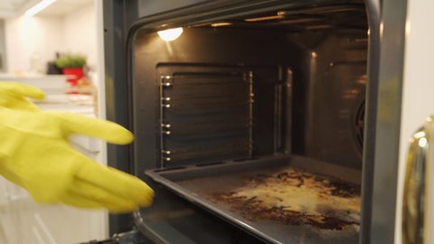 Woman wearing rubber gloves cleaning oven after cooking a fatty dish in the kitchen. Cleaning oven rack before and after. High quality 4k footage