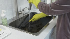 Woman wearing rubber gloves cleaning oven baking sheet in kitchen sink under running water. High quality 4k footage