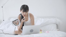Beauty of young asian woman with learning makeup with lipstick on mouth watching laptop computer with tutorial course online on bed, female teaching and explain make up with cosmetic on streaming.