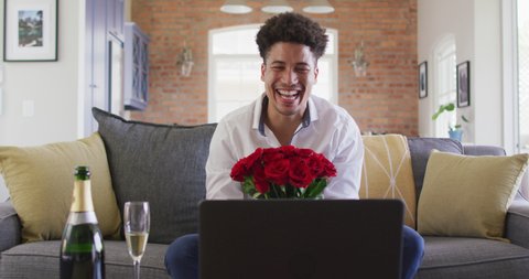 Happy biracial man with red roses making valentine's day video call on laptop. valentine's day celebration, romance and communication technology.