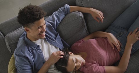 Happy biracial couple sitting on sofa in living room embracing. quality time, relaxing together at home.