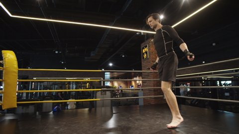 Closeup sporty male boxer exercising with skipping rope in sport club. Young fitness man jumping with jump rope on boxing ring. Energetic sport man making jumps at gym.