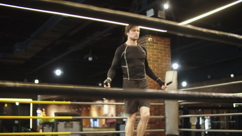 Serious fitness man jumping on rope in sport club. Closeup strict male boxer using skipping rope on boxing ring. Handsome sport man warming up before fight at fitness center.