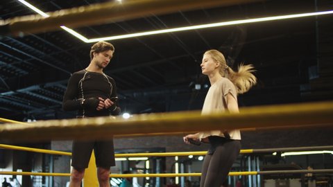 Focused coach giving advices to fit girl on boxing ring. Closeup young female athlete exercising with jumping rope in sport club. Sporty girl using skipping rope at gym.