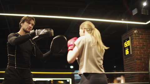 Wicked female boxer hitting punching pads on boxing ring. Sporty fit girl training with coach in sport club. Closeup serious sport couple boxing at gym.