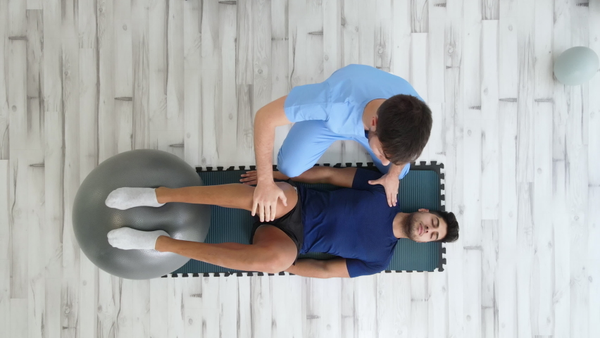 Overhead view of a Therapist Assisting Male Patient While doing exercises with a Yoga Ball at rehabilitation clinic. High quality 4k footage | Shutterstock HD Video #1082878366