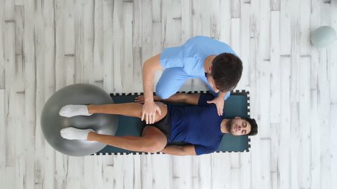 Overhead view of a Therapist Assisting Male Patient While doing exercises with a Yoga Ball at rehabilitation clinic. High quality 4k footage