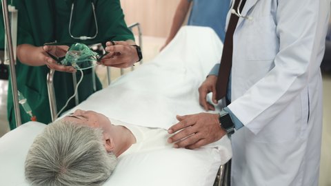 Doctor in protective equipment puts on oxygen mask to connect elderly woman patient lying in bed at hospital, anesthesiologist with mask, Patient in scrub cap with mask ventilation
