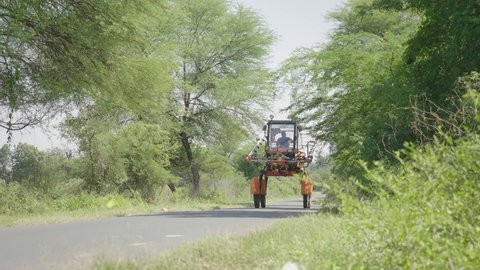 Frontal shot of a farmer driving boom pesticides sprayer vehicle or fertilizer spraying agricultural machine running on a road in South Asian region. Concept of modern agriculture or farming