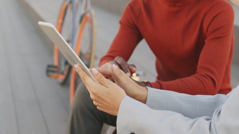 Midsection slowmo shot of hands of unrecognizable interracial business couple gesticulating while discussing work outdoors. Businesswoman holding digital tablet, showing presentation to her colleague