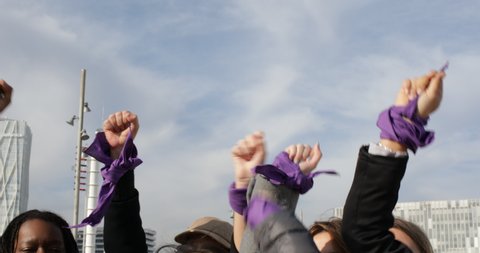 group of women with raised fists shouting slogans in feminist protest. women with purple scarf on wrist shouting slogans in feminist protest against sexist abuse.