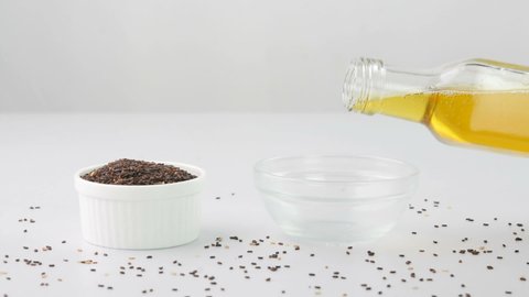 Pouring sesame oil in a cup with sesame seeds in a bowl.