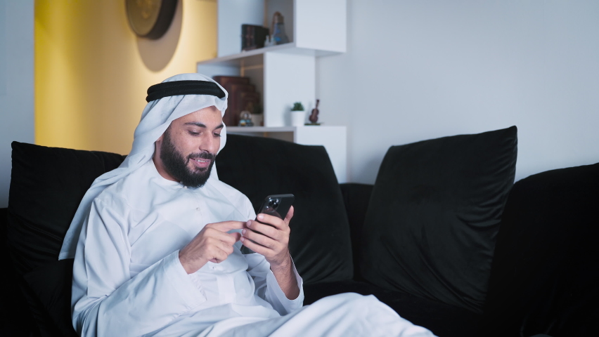 Arab Man wearing white kandura using his mobile at home Royalty-Free Stock Footage #1082888854