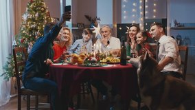 Happy caucasian family celebrating Christmas, sitting at the dinner table. Beautiful smiling family making selfie or video call with a smartphone to friends or relatives during family meal.