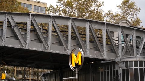PARIS, FRANCE - OCT 31, 2021: Yellow sign and subway metro train goes on outdoor part of a rout on the steel bridge over street road