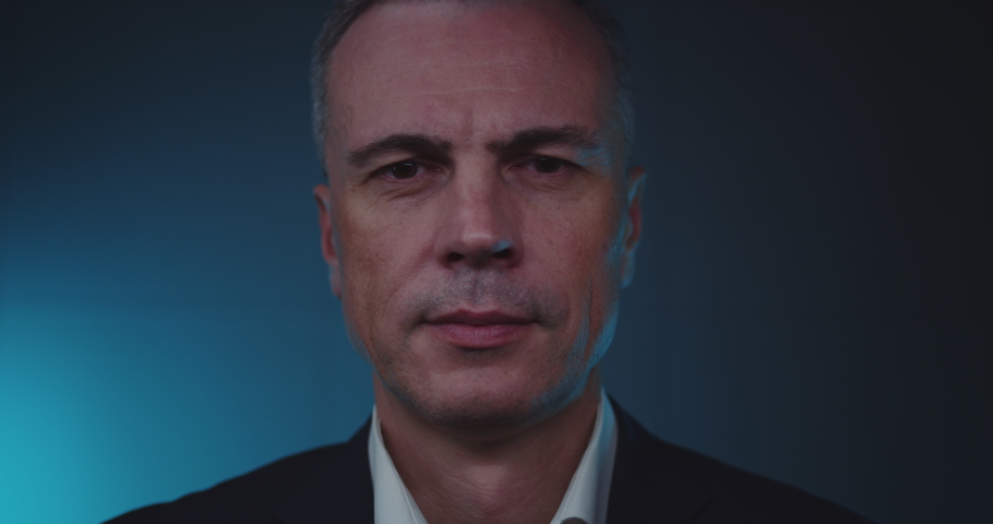 Middle aged businessman looking at camera while using futuristic face recognition system against dark blue background Royalty-Free Stock Footage #1082892544