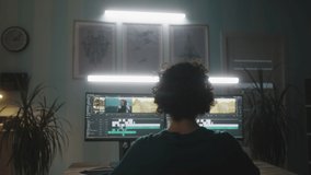 Pan right view of anonymous man with curly hair editing video on computer while working on remote project in dim workplace at home