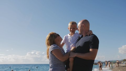 Portrait of a happy family at sea on the beach, they walk along the shore and hug. Family on vacation at the sea