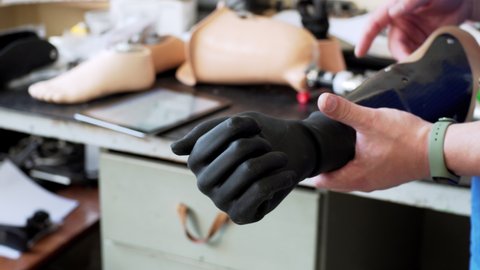 A medical prothetics techinican demonstrates black modern artifical bionic arm prothesis in the laboratory moving its fingers. An artificial hand moves black fingers