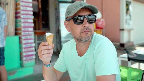 A man in sunglasses sits and eats ice cream.