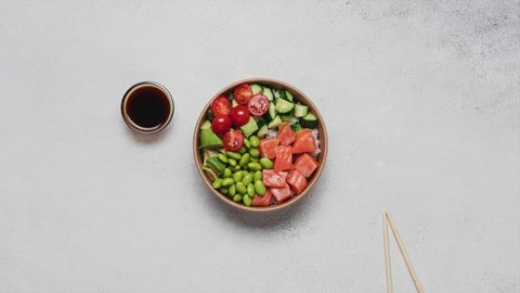 Stop motion animation of cooking poke bowl. Salmon, avocado, cucumber, tomato, edamame beans and rice poke bowl on white background