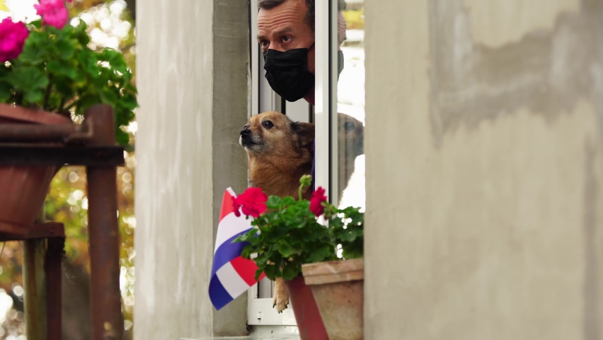 Covid-19 lockdown in Netherlands. Sad Dutch man with dog on home balcony. Flag of Netherlands. Self-isolation in quarantine, lockdown, stay at home, social distancing