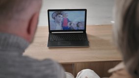 elderly couple together communicates with their family remotely using laptop at home, gray-haired grandparents use modern technologies, over shoulder view