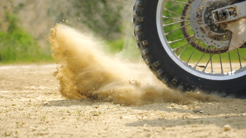 Close up wheel of powerful off-road motorcycle starting movement. Motocross bike starts move. Dry ground or dust flying around. Concept of motorsport or active lifestyle. Slow motion Side view