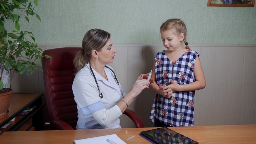 A female doctor in a white coat vaccinates a school-age girl who is very afraid. Mass vaccination of children. Royalty-Free Stock Footage #1082905381