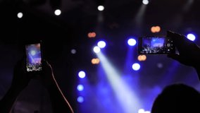 Slow motion: people hands silhouette taking photo or recording video of live music concert with smartphone. Bright colorful stage lighting. Nightlife, technology, photography, entertainment concept