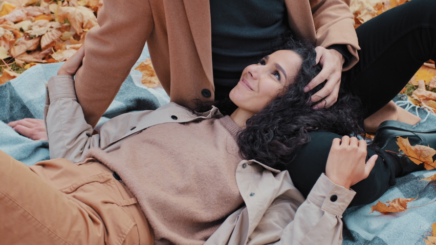Young hispanic girl in love lie on blanket in autumn park unrecognizable man stroking woman on head lady with thick curly hair guy taking care of beloved girlfriend couple spend time together outdoors