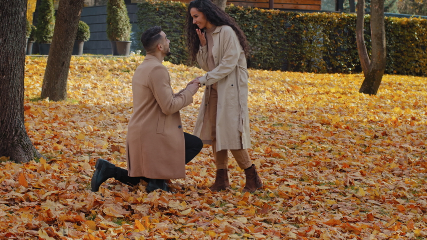 Hispanic loving couple in autumn park man stand in yellow leaves on one knee making marriage proposal girlfriend and puts ring on finger excited happy woman jump and tight hugs sweetheart guy outdoors Royalty-Free Stock Footage #1082913790