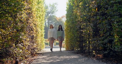 Young women does defile in slow motion the park. Fashion stylish video of two girls in short skirts walking to the camera outdoors, 4k 60p Prores HQ