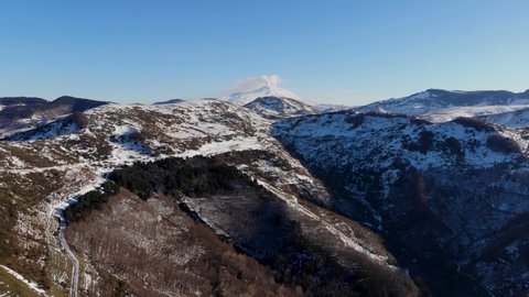Aerial shot with drone of the Nebrodi mountains in winter with a view of smoking Etna and Lake Pisciotto. Winter in Sicily. Snow in Sicily. Snow-capped Etna. Iced lake.