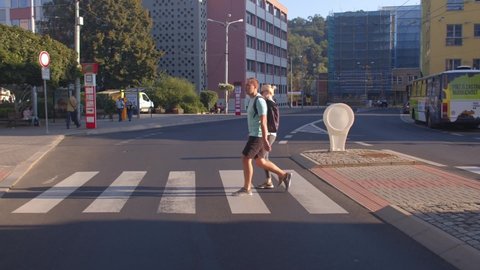 A couple of man and woman are moving along the pedestrian crossing in the city. Bus movement. Sunlight. CZ, Usti nad Labem, Socialni, 15.9.2021 