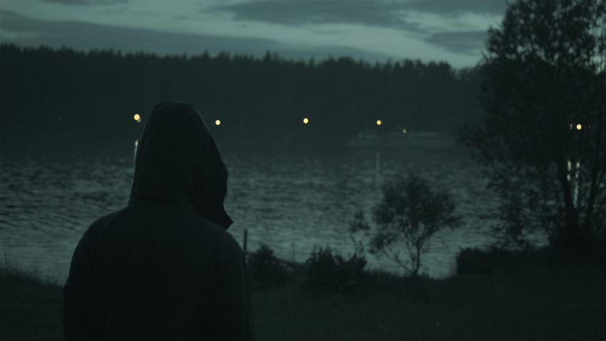 A mysterious man in the forest, on the coast looks in the evening at the lights of glowing houses Royalty-Free Stock Footage #1082919406
