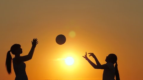 Mom and daughter play volleyball with a ball in the park at sunset, silhouette. Happy family playing with a ball on the beach at sunset. Happy family and childhood concept. Summer family camping